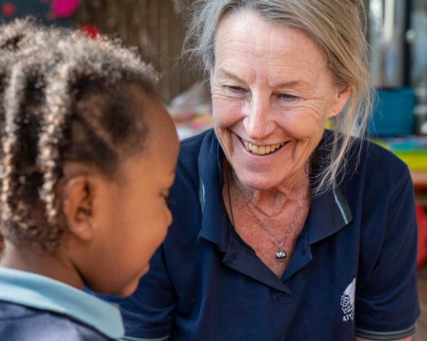 Woman in a blue shirt smiling and interacting with a child outdoors