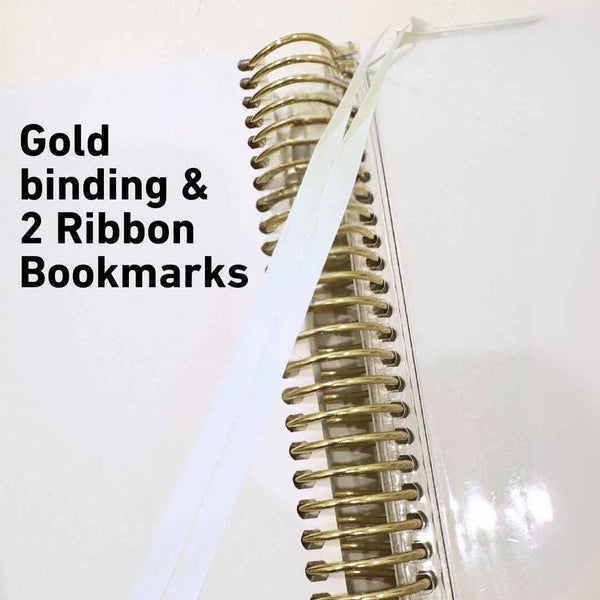 White notebook with gold binding and ribbon bookmarks on a white background