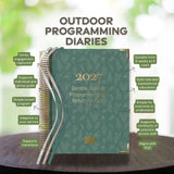 Green programming diary with text on a wooden surface and blurred greenery in the background
