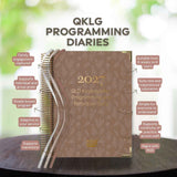 2027 QLKG Programming Diaries on a wooden surface with greenery in the background