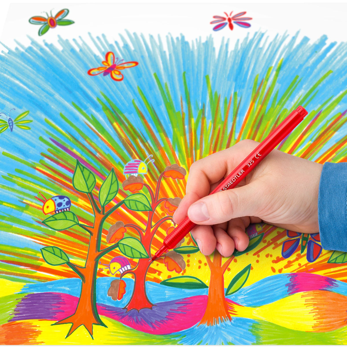 Hand holding a red marker coloring a vibrant, child-like drawing of trees and butterflies.