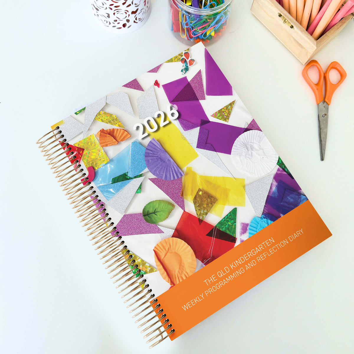 The QLD Kindy Weekly Programming and Reflection Diary for QKLG with the Child Artist Cover on a QLD Kindergarten Teacher's desk