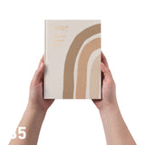 Hands holding a 2027 educator planner with a beige and brown design on a white background