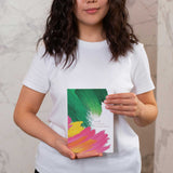Person wearing a white t-shirt holding a colorful book with a green, yellow, and pink design.
