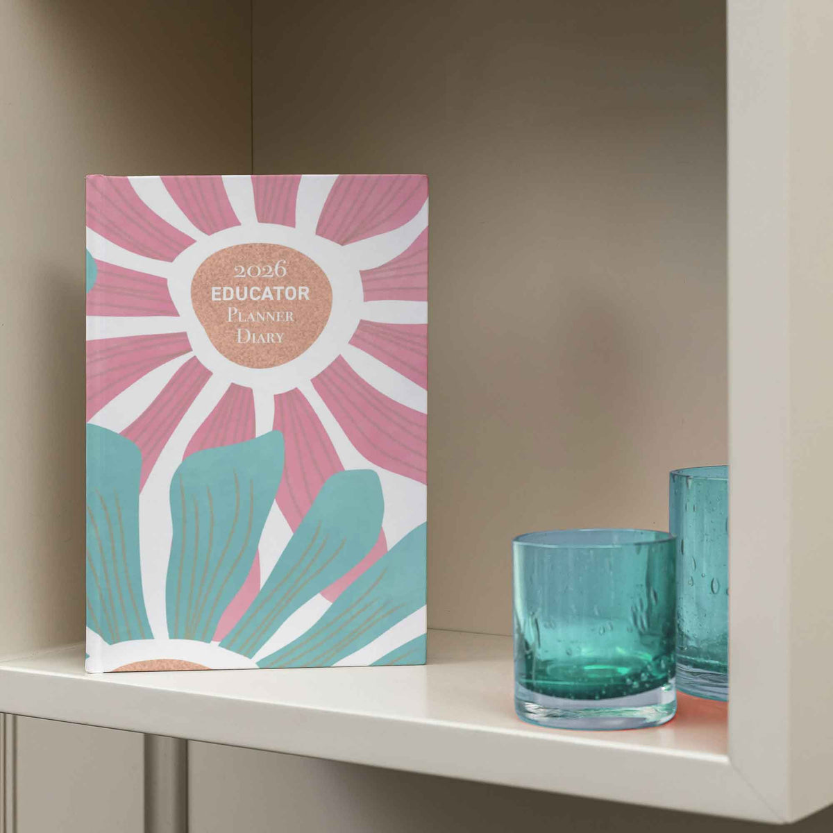 Planner diary with pink and blue design on a shelf with two green glasses.