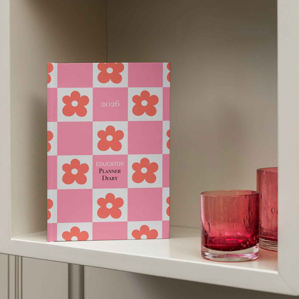 Pink and white checkered planner with floral patterns on a shelf with red glasses.