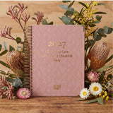 2027 Family Day Care Compliance Checklist Diary on a wooden surface with flowers