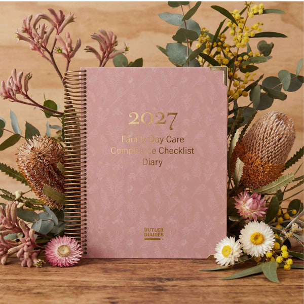 2027 Family Day Care Compliance Checklist Diary on a wooden surface with flowers