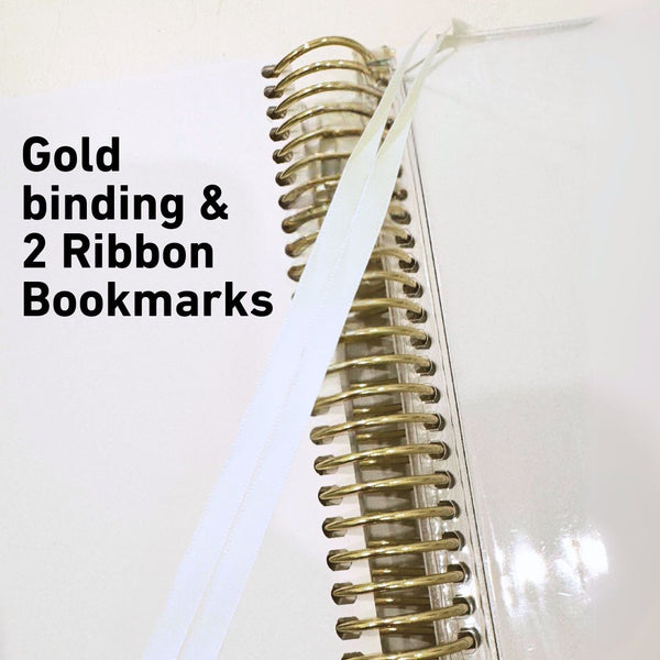 White notebook with gold binding and ribbon bookmarks on a white background