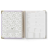 Open spiral-bound planner with floral pattern on one page and text on the other, on a white background.