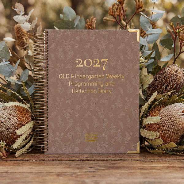 2027 QLD Kindergarten Weekly Programming and Reflection Diary on a wooden surface with decorative plants.