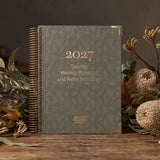 2027 Teacher Weekly Planning and Reflection Diary on a wooden surface with plants.