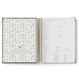 Open spiral-bound book with floral pattern on one page and text on the other, on a white background.
