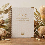 2027 weekly programming and reflection diary with floral decorations on a wooden surface