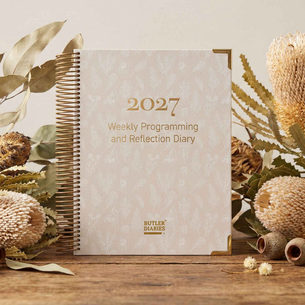 2027 weekly programming and reflection diary with floral decorations on a wooden surface