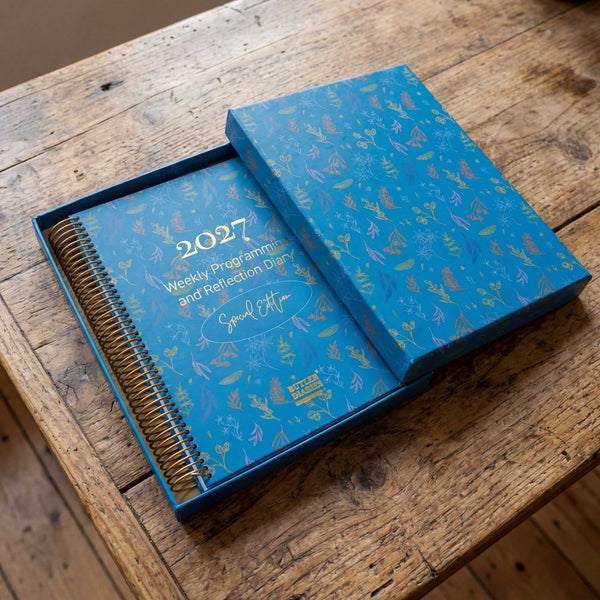 Blue weekly program diary in a gift box with 2027 on a wooden surface