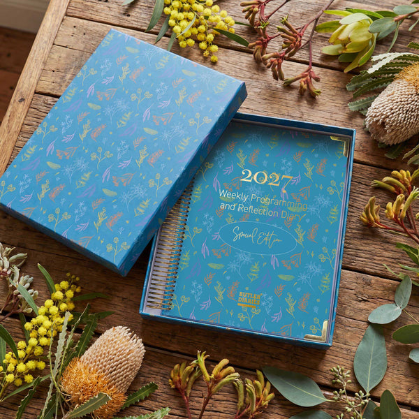 Blue special edition weekly planner with floral design on a wooden surface with flowers around